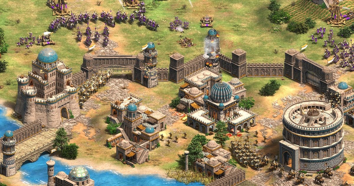 Age of Empires II: Definitive Edition battle where purple cavalry and siege weapons surround and attack a walled city with a blue domed castle and a round amphitheater