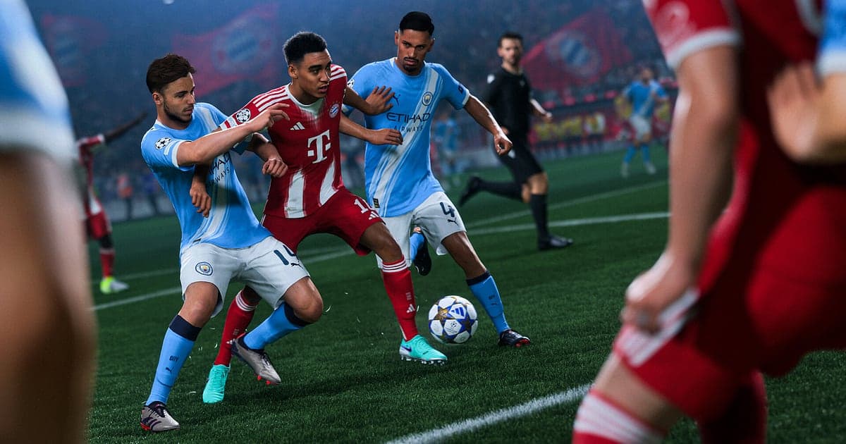 Partido de EA SPORTS FC 26 donde un jugador con uniforme rojo protege el balón entre dos defensas de azul claro, con el árbitro y una tribuna llena detrás