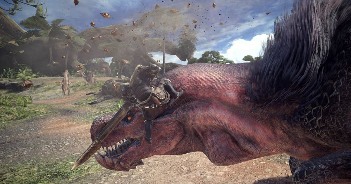 Szene aus Monster Hunter: World: Ein Jäger sitzt auf dem Kopf eines riesigen rot geschuppten Monsters auf einem Waldweg und rammt eine Klinge hinein, während Erde und Blätter aufwirbeln