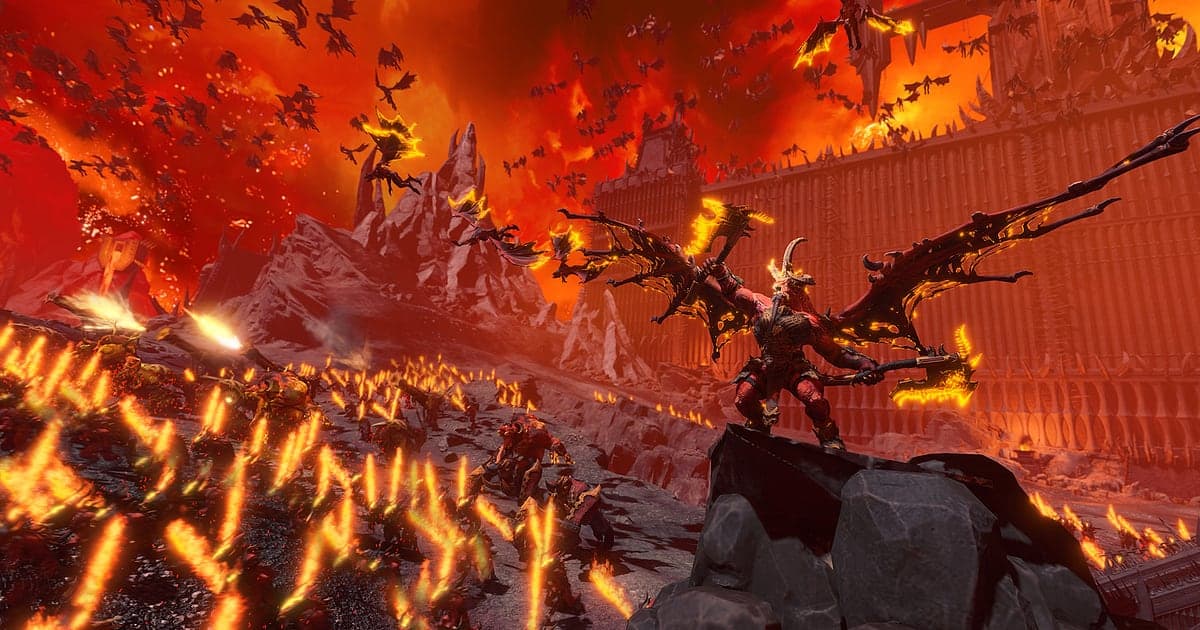 Ein geflügelter Dämonenfürst steht in Total War: WARHAMMER III unter einem brennend roten Himmel auf einem Felsen, während eine gewaltige Dämonenhorde auf eine Festungsmauer zustürmt