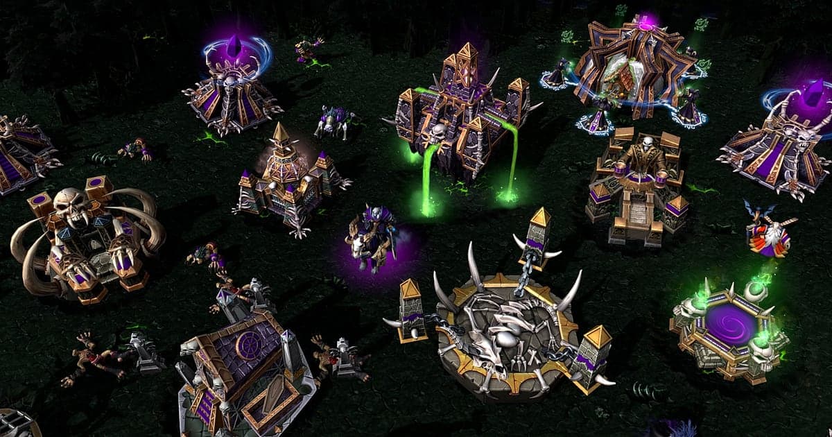 Una base de No-muertos en Warcraft III: Reforged de noche, con edificios coronados por calaveras y llamas moradas alineados entre árboles oscuros