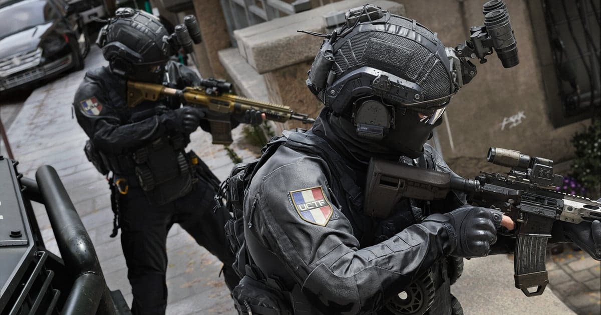 Screenshot resmi Call of Duty: Modern Warfare 4: dua operator berseragam taktis hitam dengan emblem unit tiga warna Prancis maju di jalan melewati mobil yang terparkir, senapan terangkat