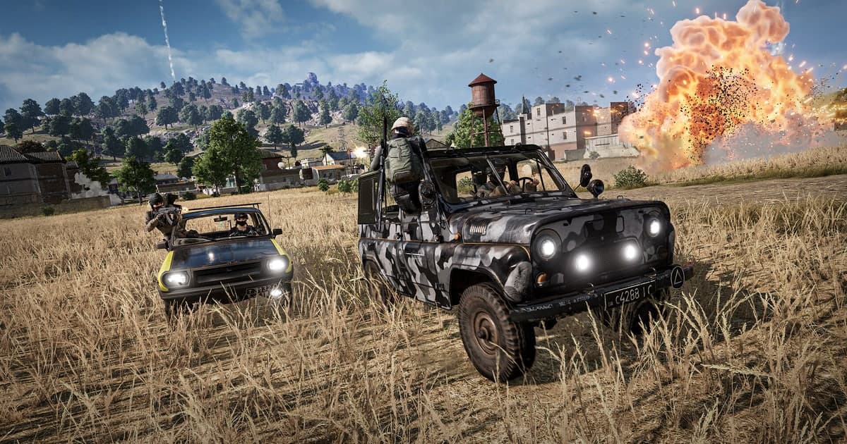 Actual PUBG gameplay — two vehicles in a wheat field with an armed player and an explosion erupting in the village to the right