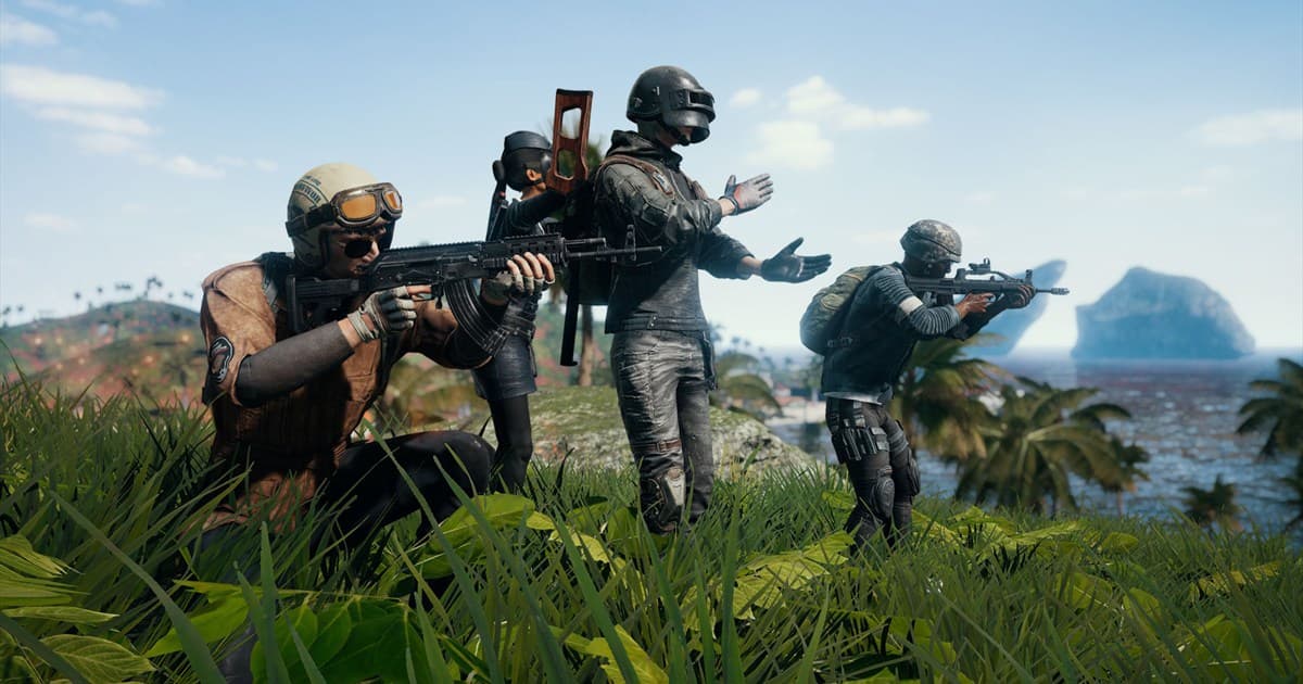 Four PUBG characters with rifles standing and crouching in a grassy coastal field