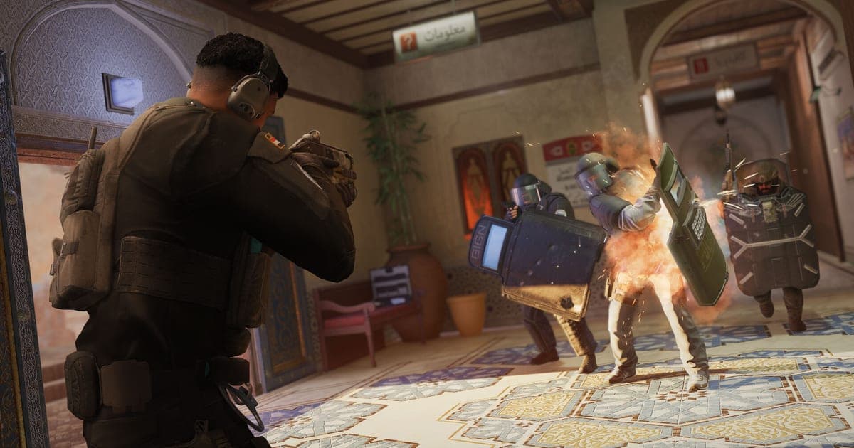 レインボーシックス シージの実際のゲーム画面 — 室内でオペレーターがシールドを持つ相手と撃ち合う交戦シーン
