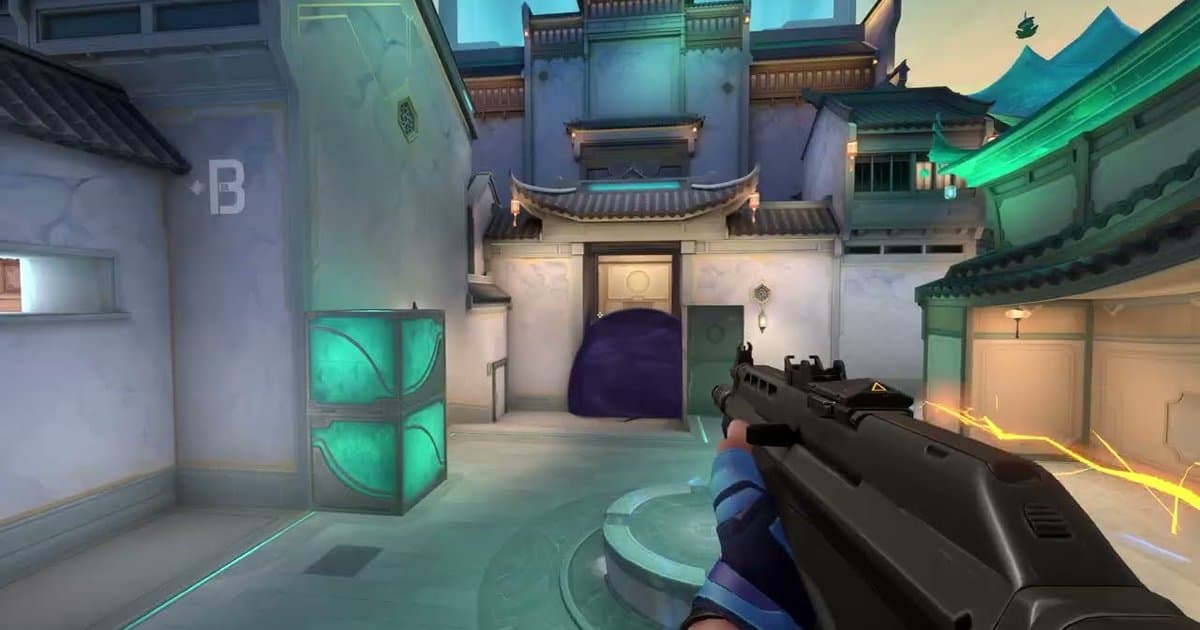 Visão em primeira pessoa do trailer oficial de gameplay de Summit do VALORANT: arma na mão num pátio com uma seta do bomb B na parede e uma smoke roxa bloqueando a porta à frente